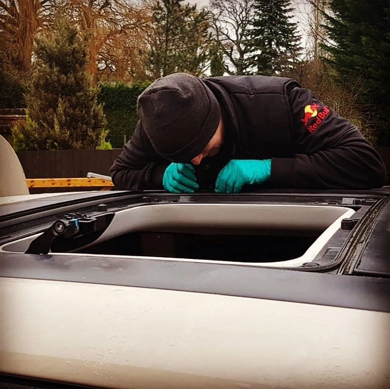 A man in a black jacket and blue gloves cleaning the hood of a car.